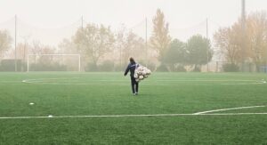 A person with a net full of soccer balls walking down a field