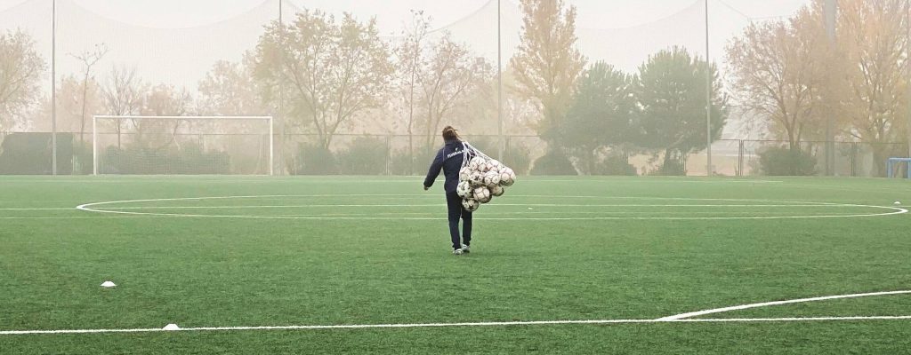 A person with a net full of soccer balls walking down a field